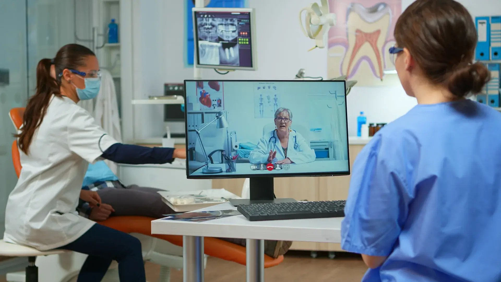 Clinicians in an exam room with a patient image on a monitor