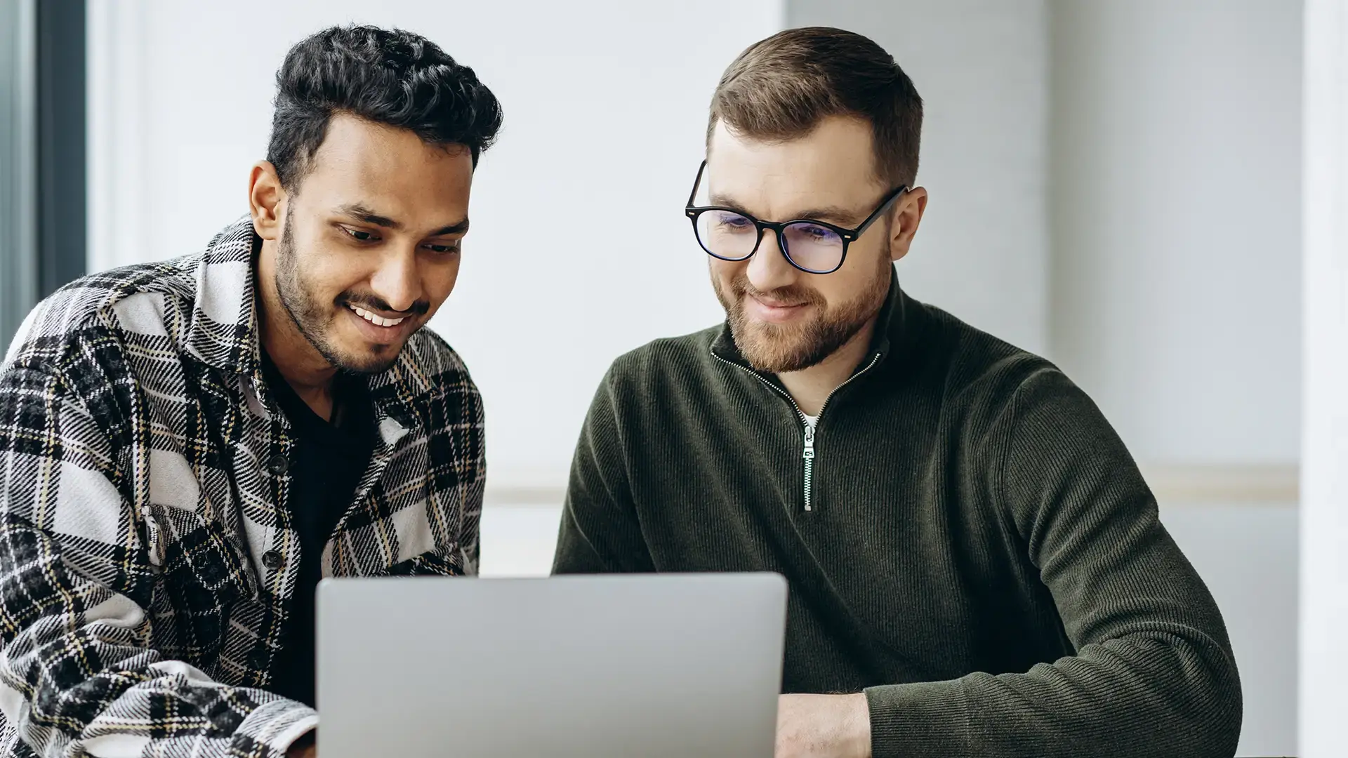 Two colleagues smiling while collaborating on a laptop in an office