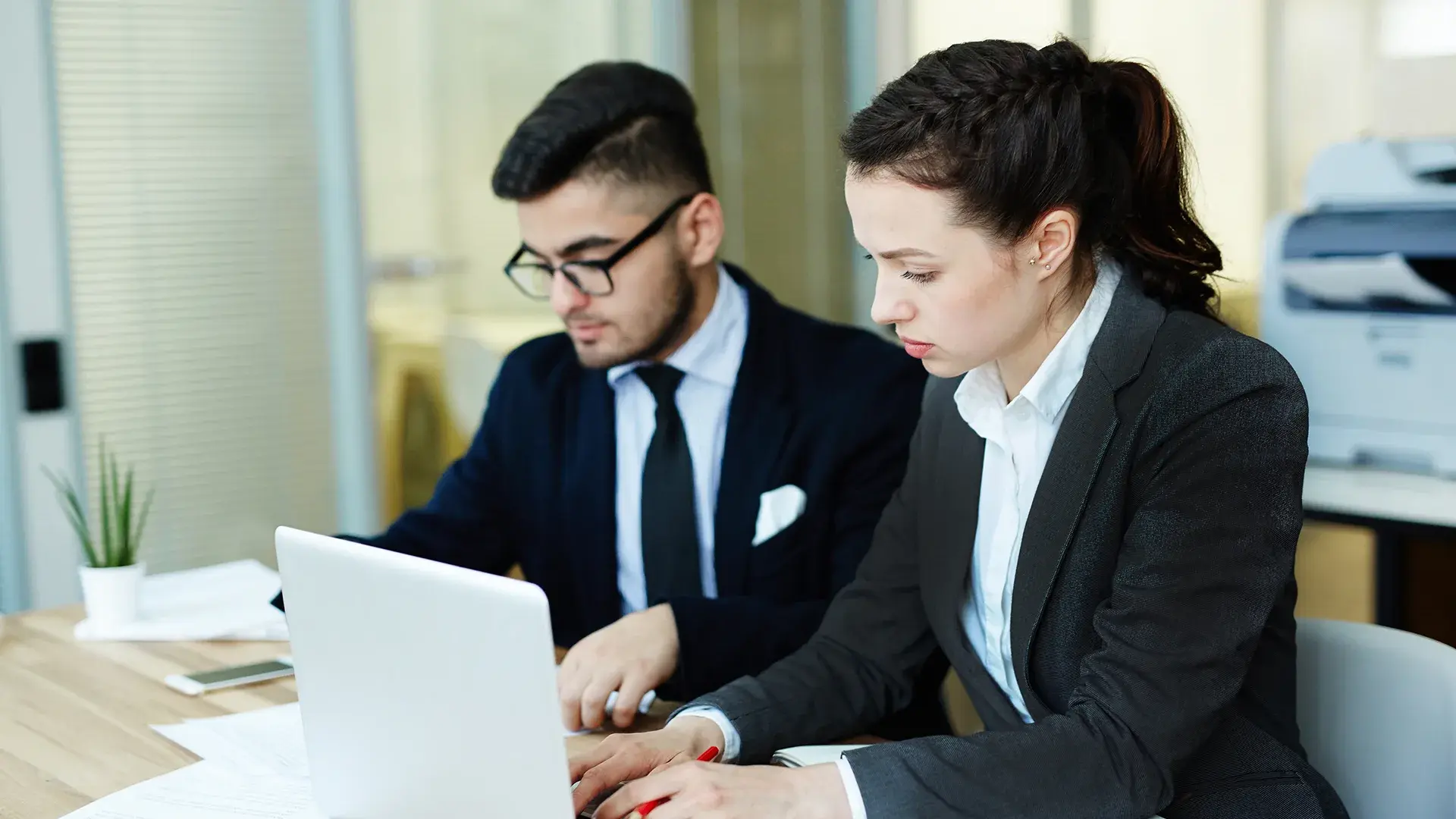 Two legal professionals reviewing documents together on a laptop in an office setting.