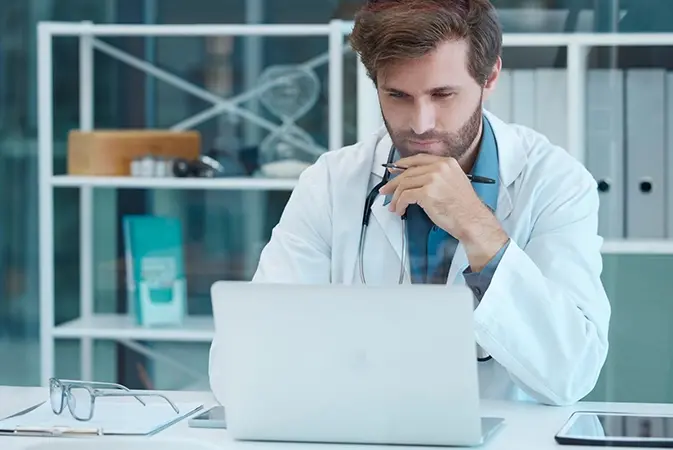 A doctor working at a laptop in a clinic office