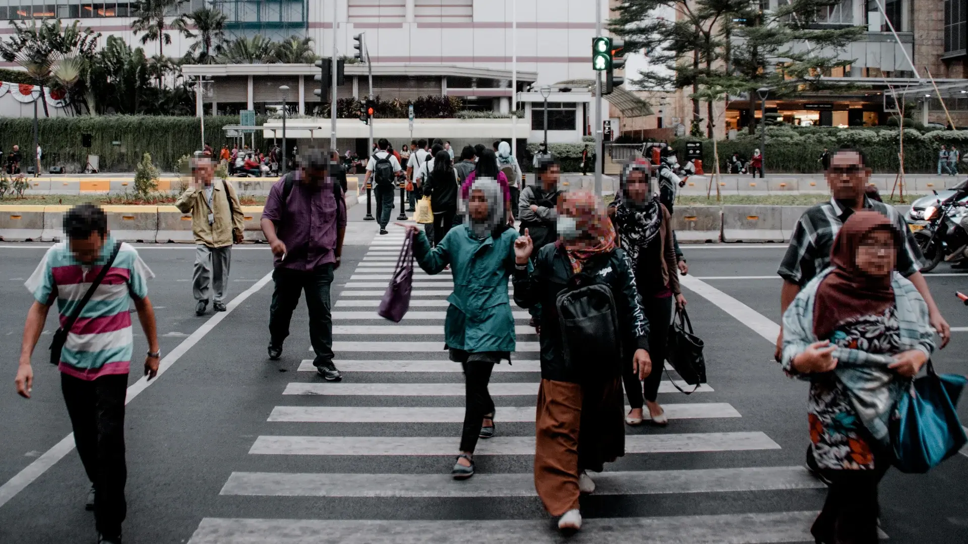 A group of people crossing a city street at a pedestrian crosswalk, with their faces blurred for privacy, demonstrating AI-powered video redaction to protect personal identities in public footage.