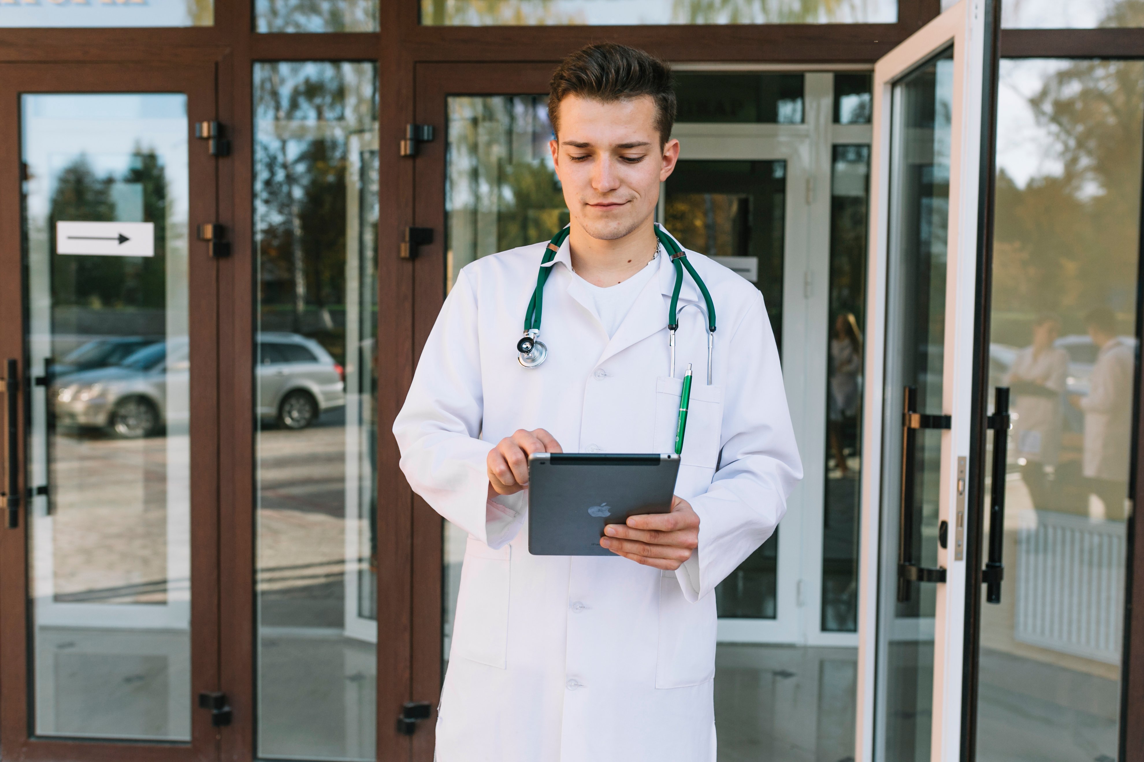 A doctor reviewing a study on a tablet at a clinic entrance